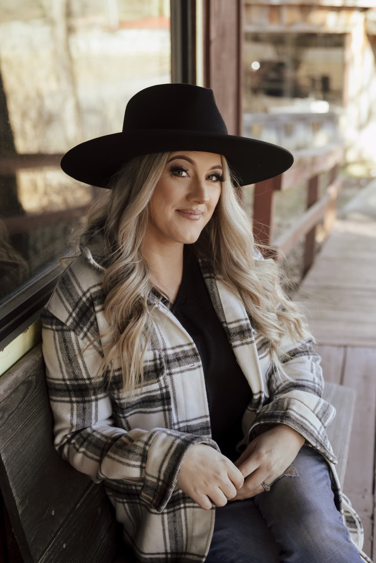 Candace Roberts seated on a porch bench in a black hat
